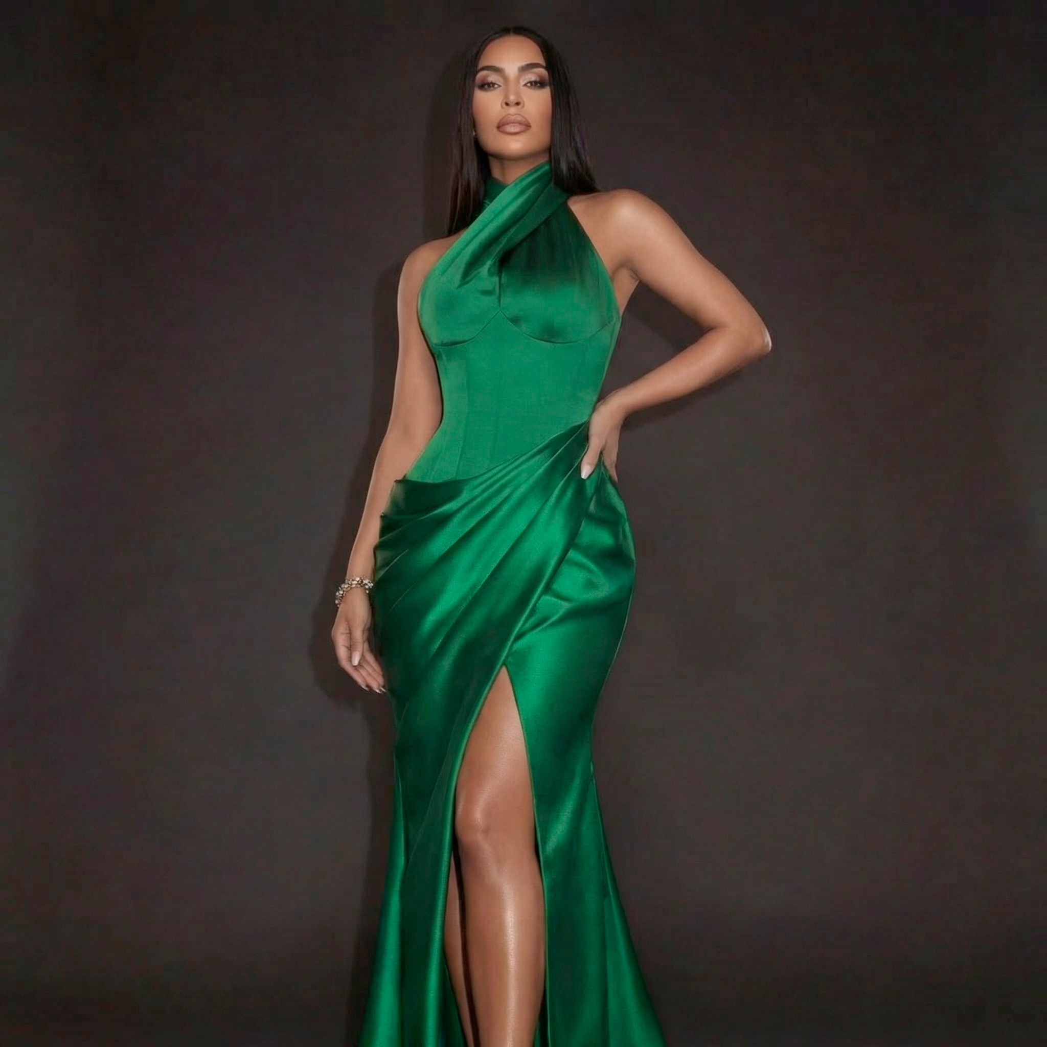 Woman wearing a green satin dress with a high slit on a dark background