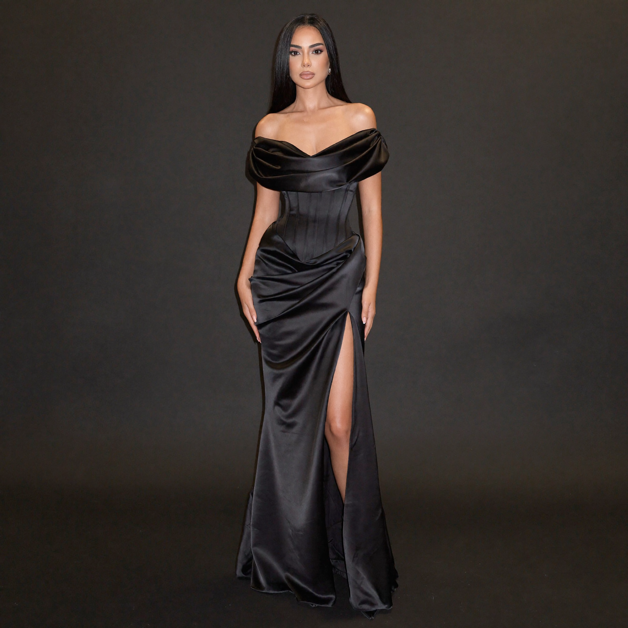 Woman wearing a black off-shoulder gown with a slit on a dark background