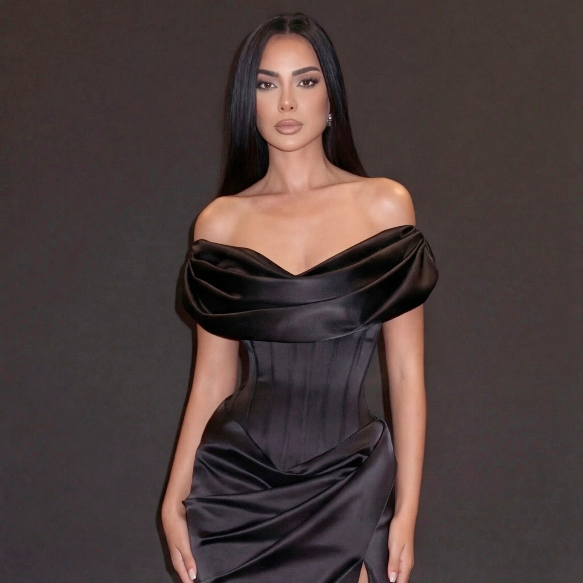 Woman wearing a black off-shoulder satin dress against a dark background