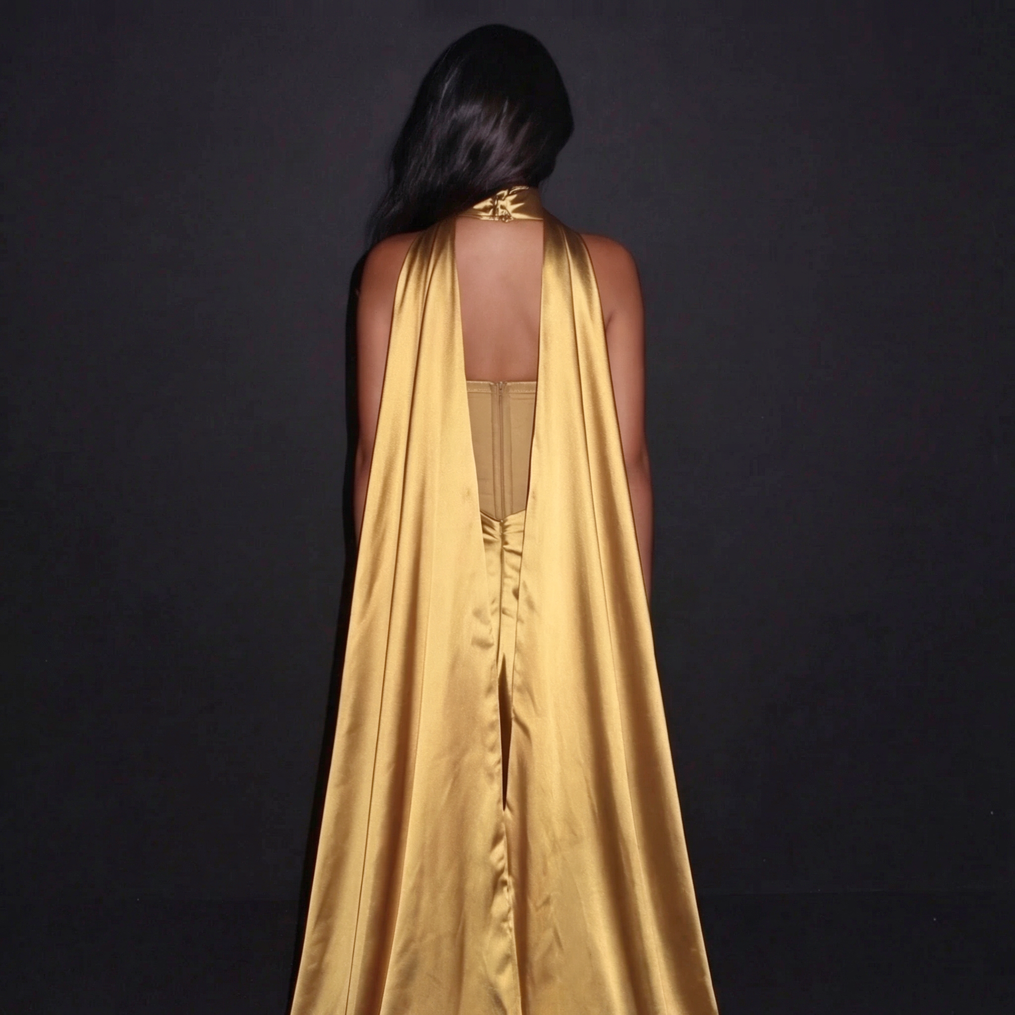 Woman wearing a gold dress with a cape against a black background